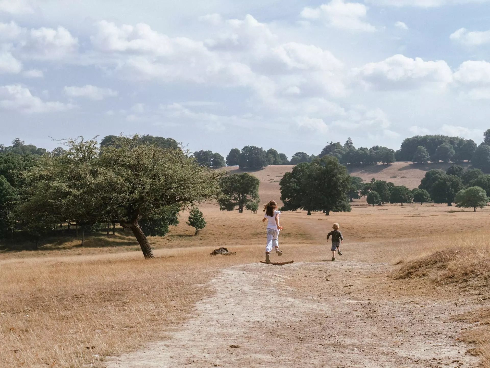 a woman and boy running on a dirt path in a field